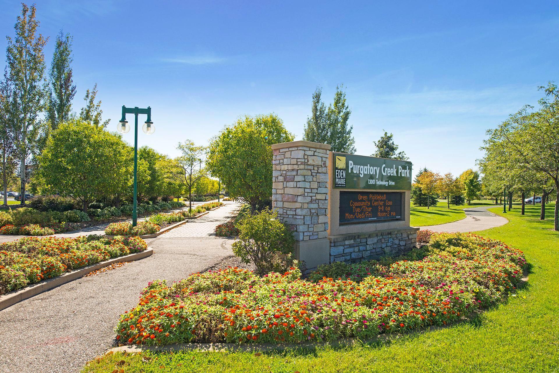 Purgatory Creek Park entrance sign beside flower beds and landscaped walking paths.