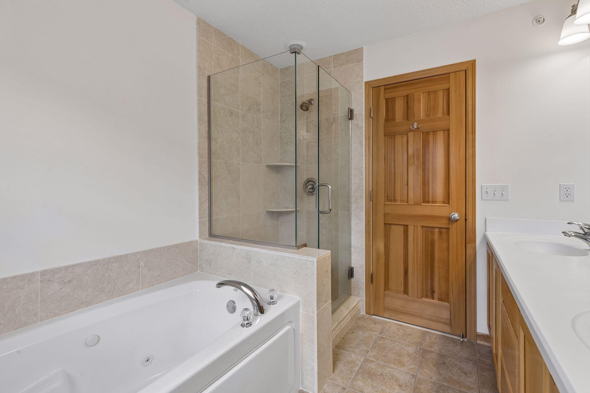 Bathroom with a jetted soaking tub beside a glass-enclosed tiled shower and wood vanity.