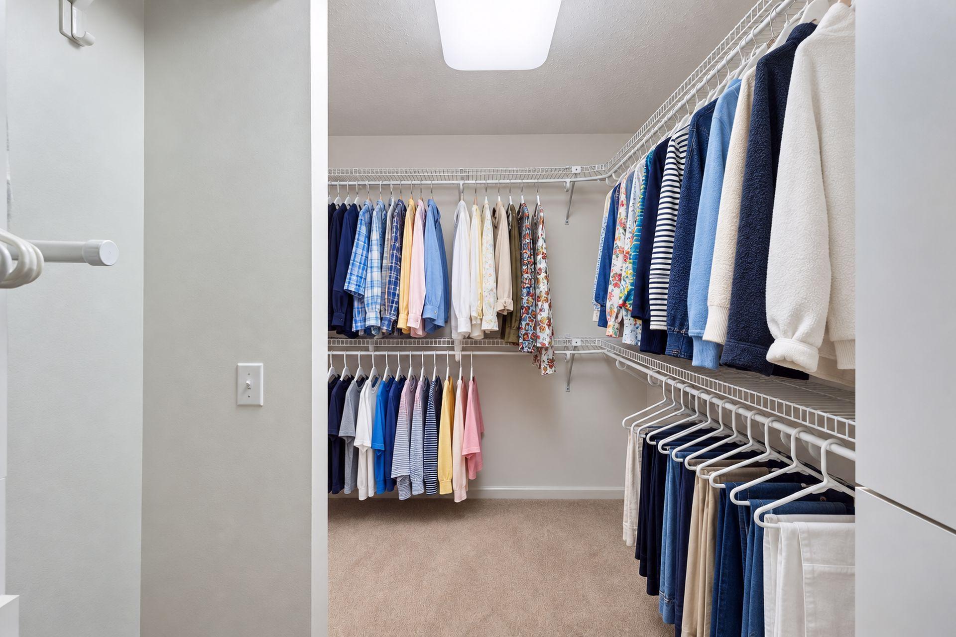 Walk-in closet with clothes hanging on white wire shelving along three walls.