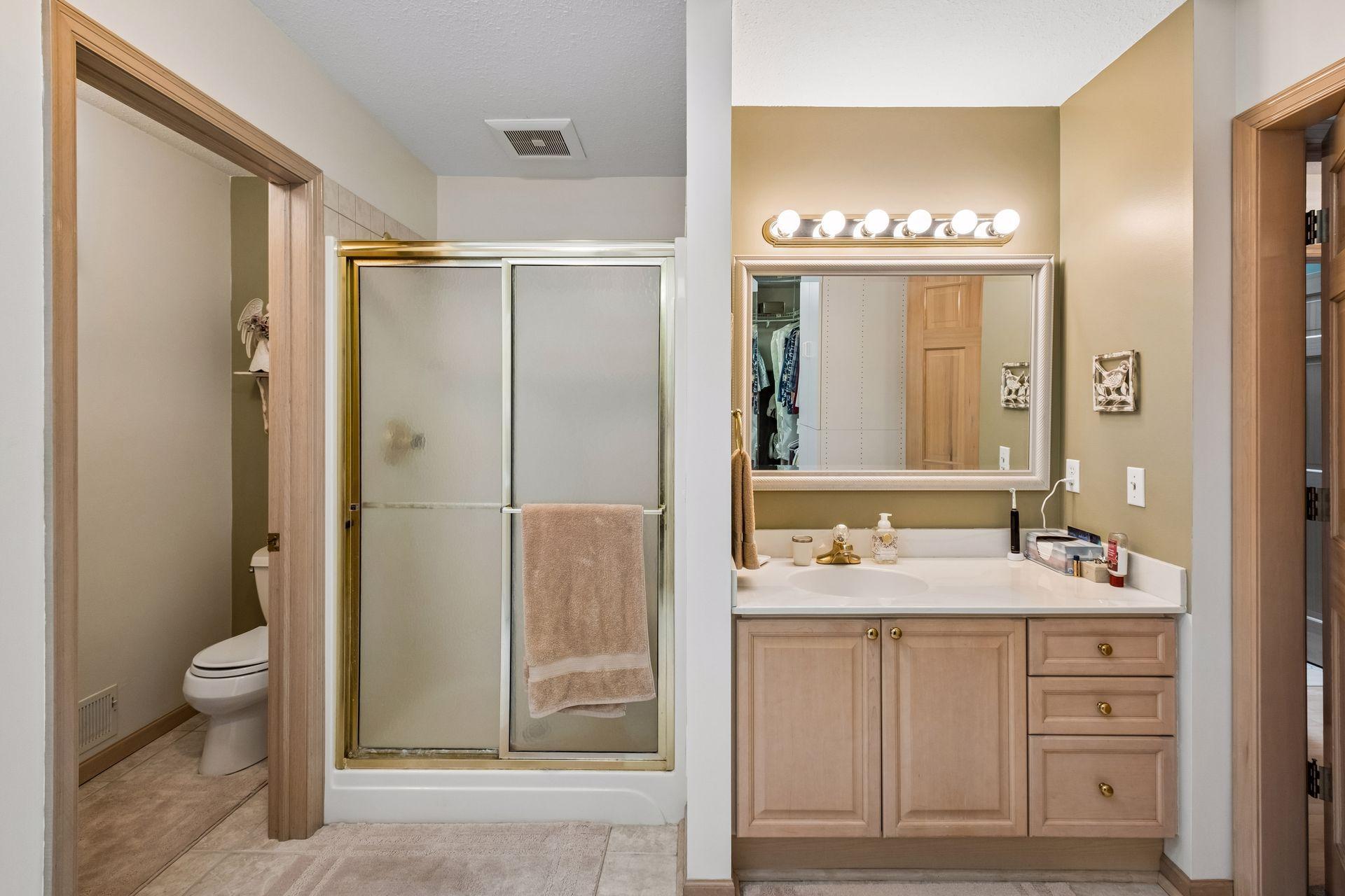 Bathroom with a glass shower and light wood vanity beneath a large illuminated mirror.