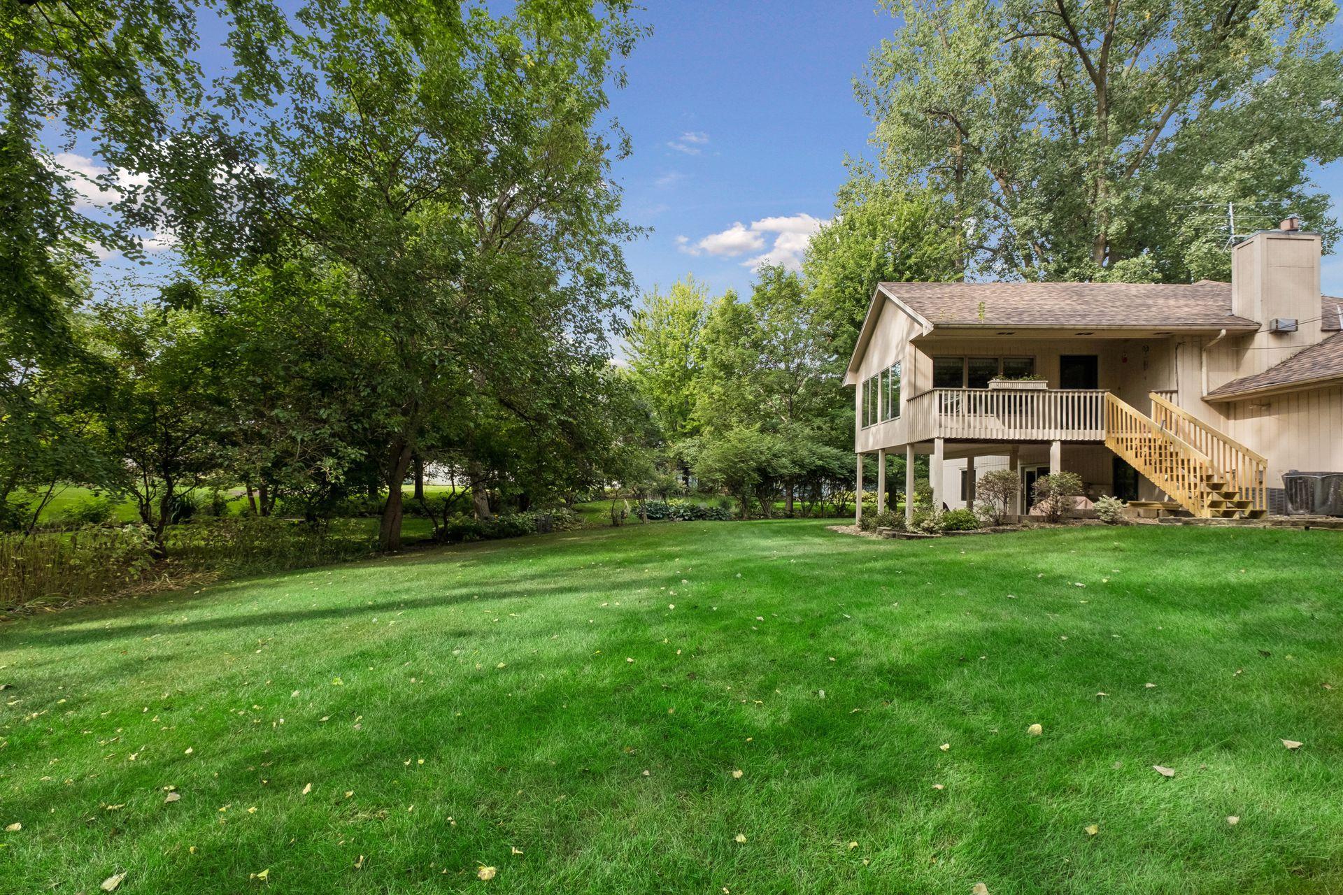 Home’s rear exterior with an elevated deck, wooden stairs, mature trees, and a broad lawn.