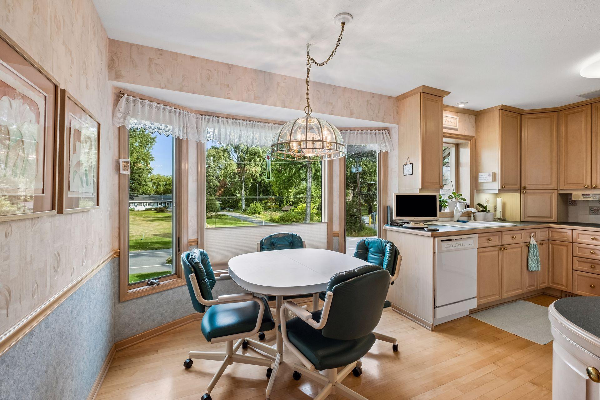 Kitchen dining nook with teal chairs, a round table, and large windows overlooking greenery.