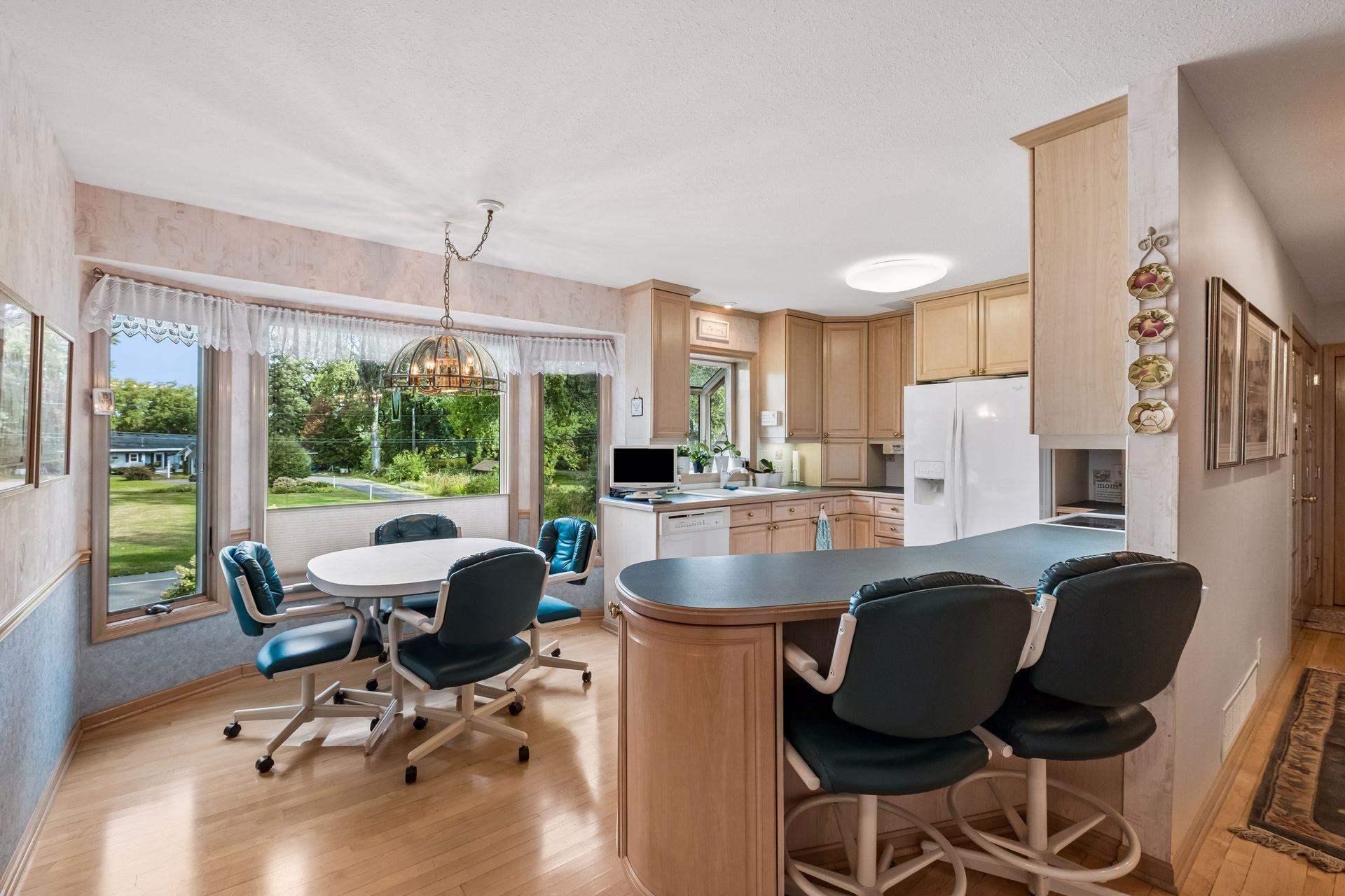 Kitchen and dining area with a curved dark-countertop island, light wood cabinets, and large yard-facing windows.