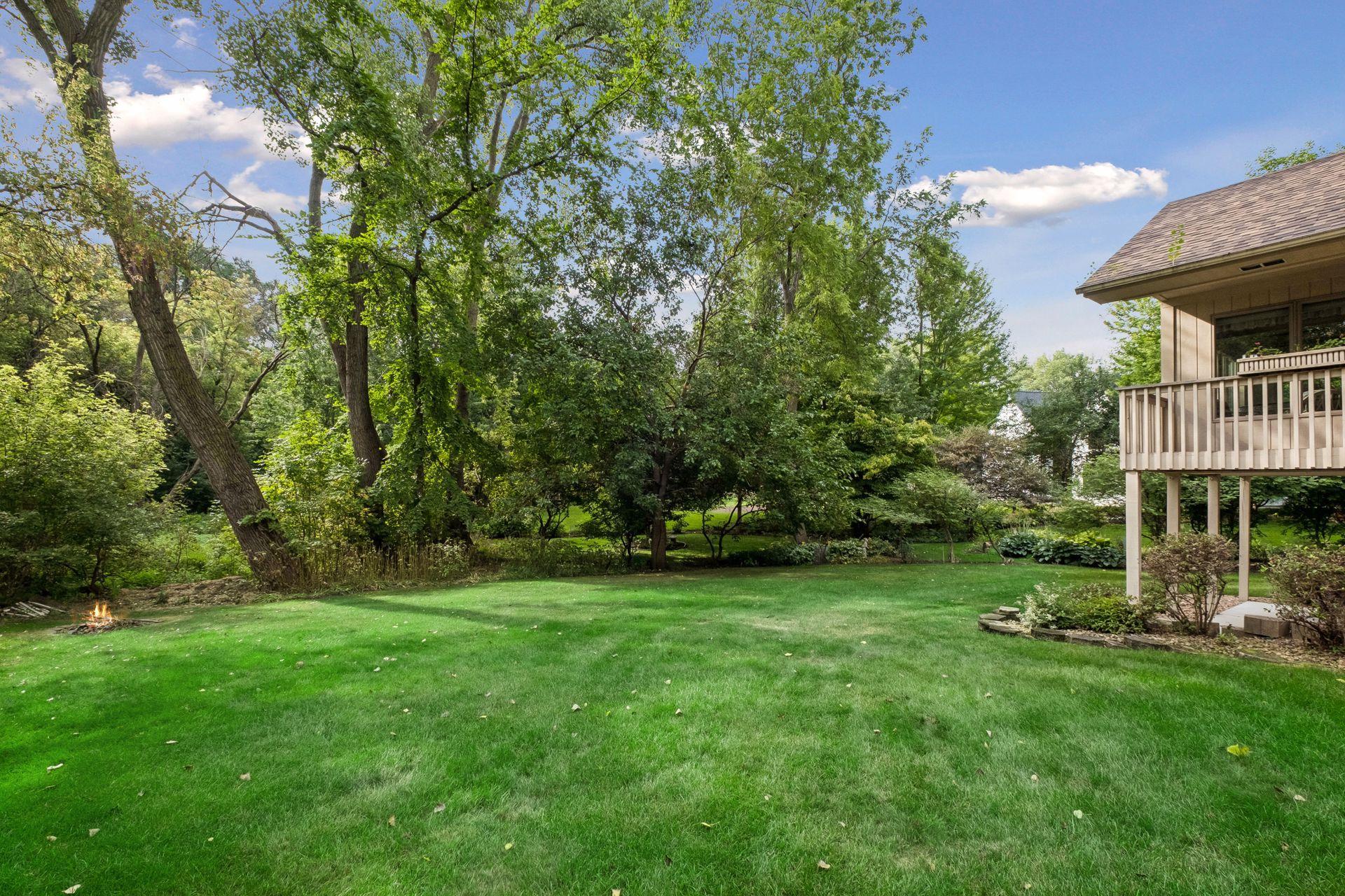 Backyard with a broad lawn, mature trees, raised deck, and small fire pit.