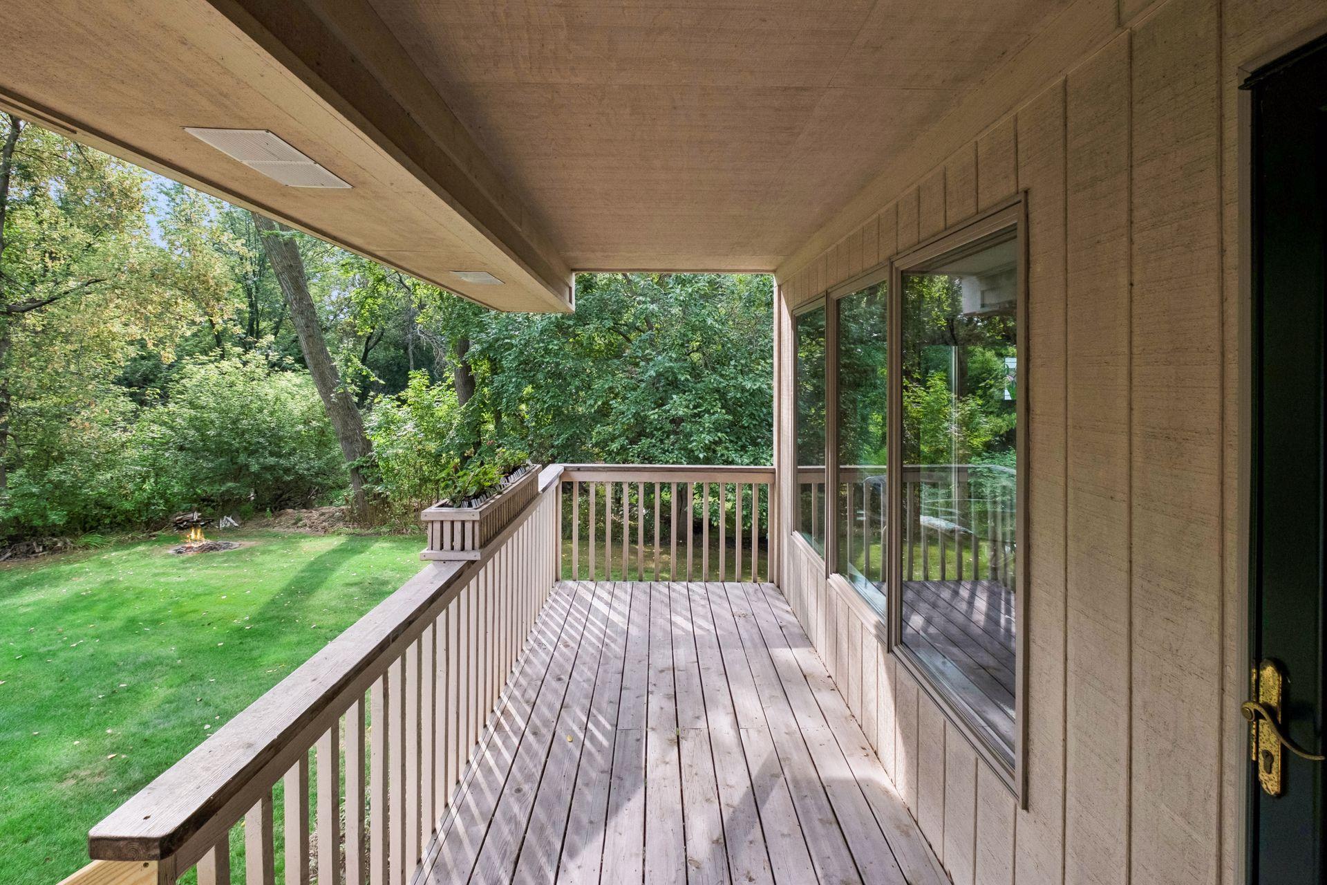 Covered wooden deck overlooking a green lawn, fire pit, and wooded yard.