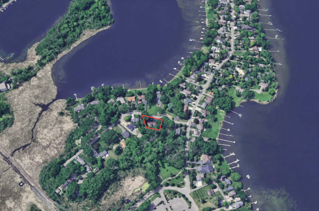 Aerial view of a wooded lakeside neighborhood, with a red outline marking one property.