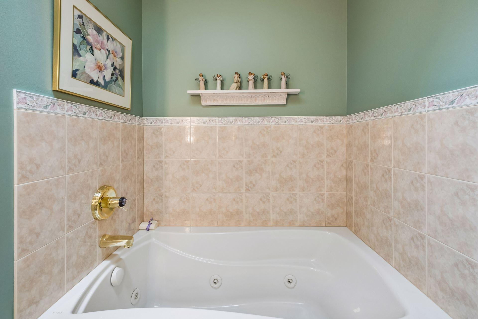 Bathroom jetted tub with beige tile, green walls, and gold-tone fixtures.