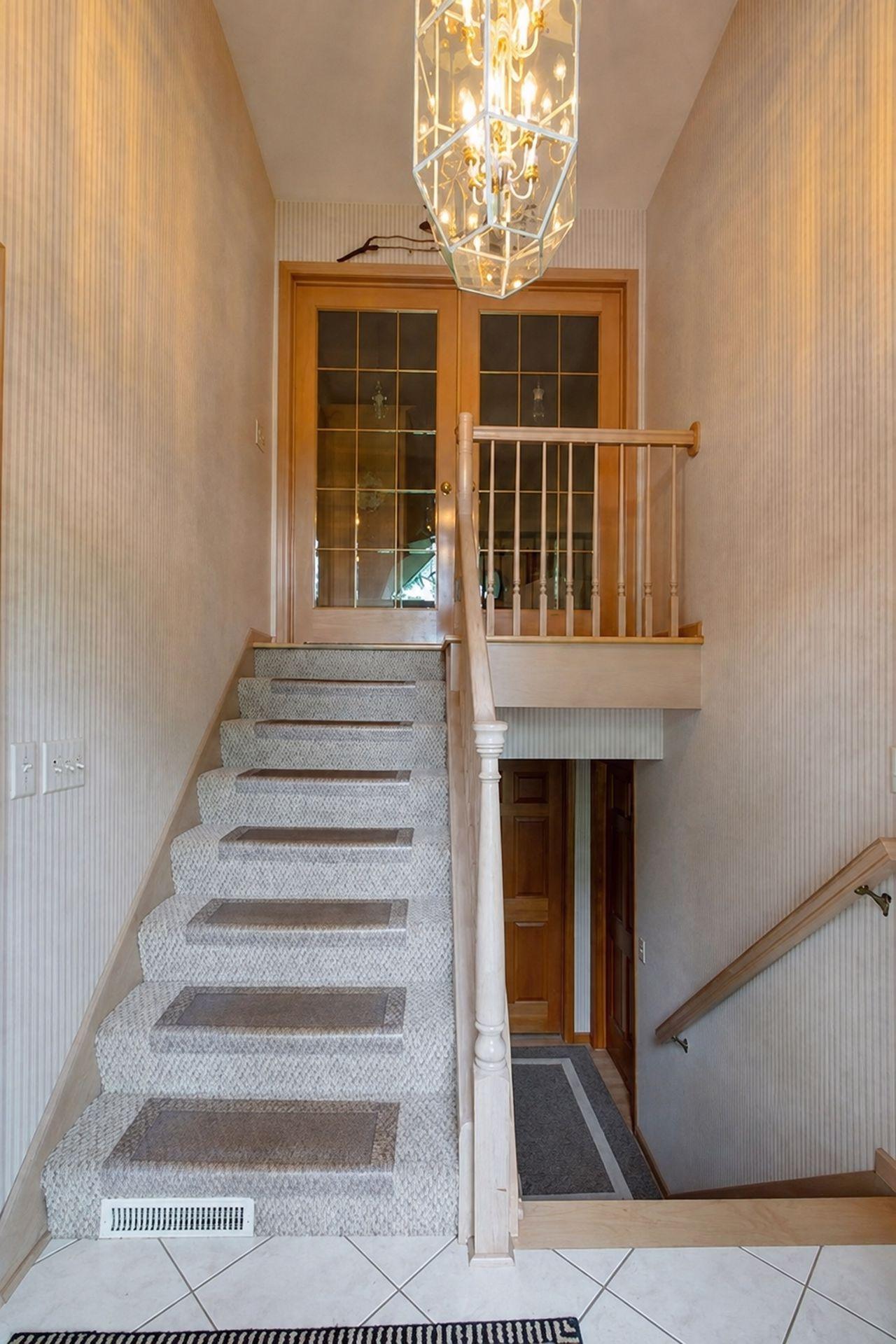 Foyer staircase with carpeted steps, wooden banister, glass-paneled doors, and a large chandelier.