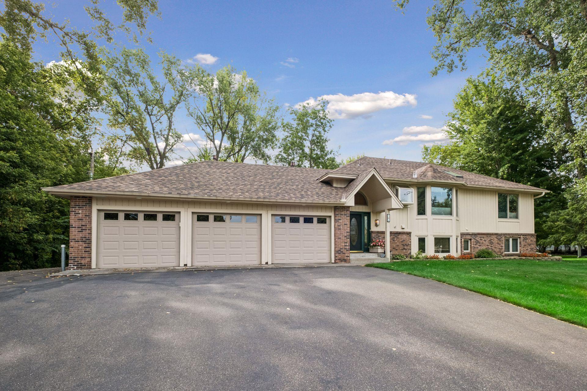 Split-level house with a three-car garage, brick accents, and a landscaped lawn.