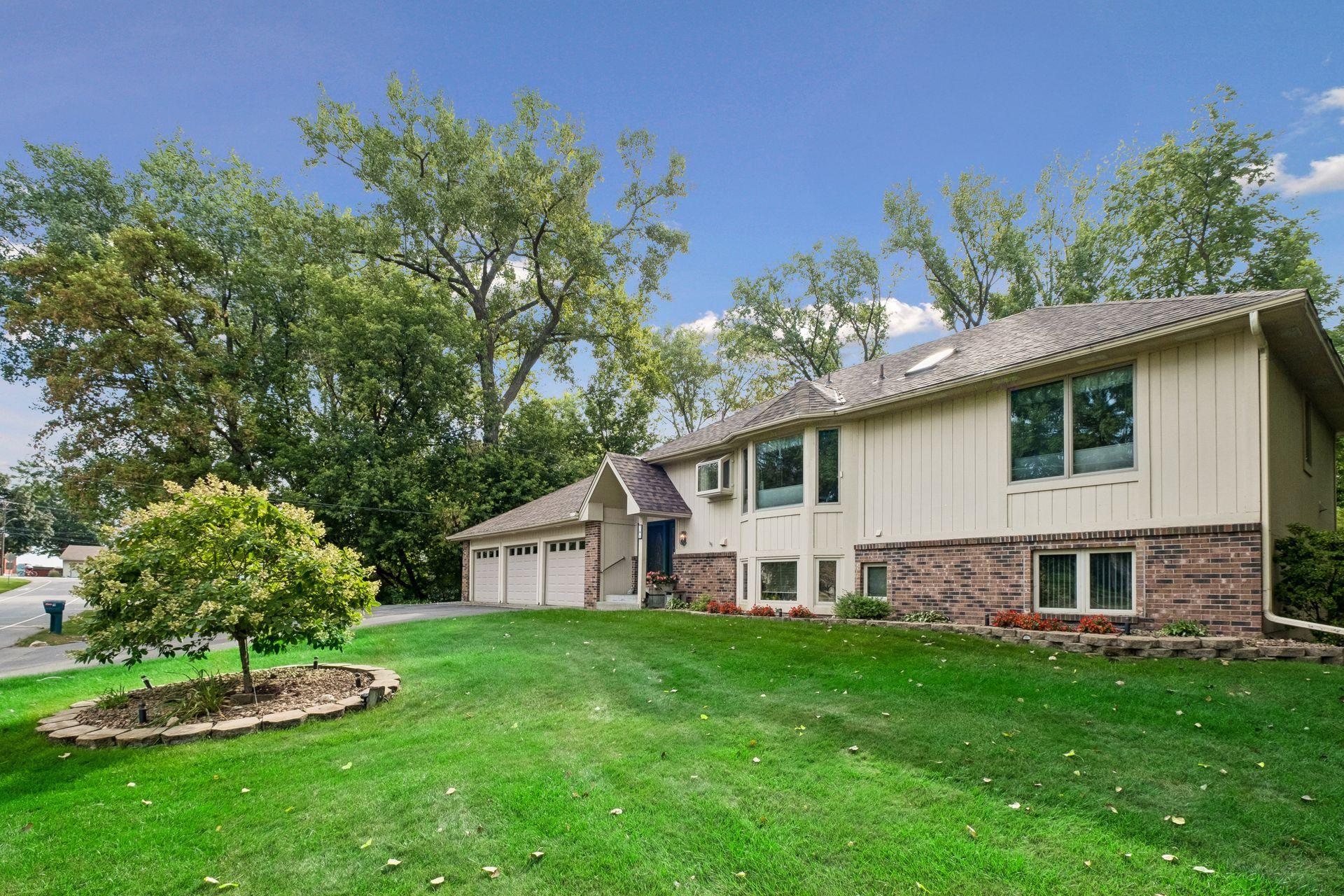 Split-level house with brick and light siding, an attached two-car garage, and a leafy lawn.