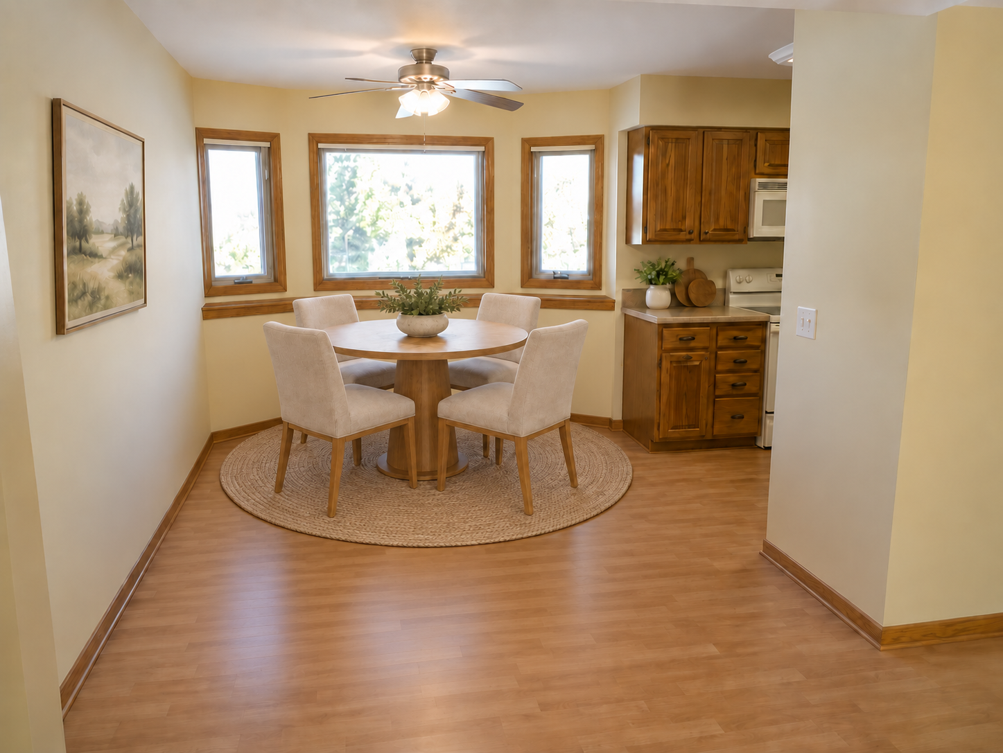 Dining nook with a round wood table, four upholstered chairs, and three bright windows.