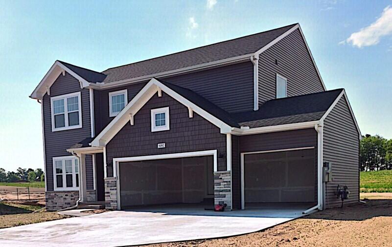 Two-story gray house with white trim, stone accents, and a wide three-car garage.
