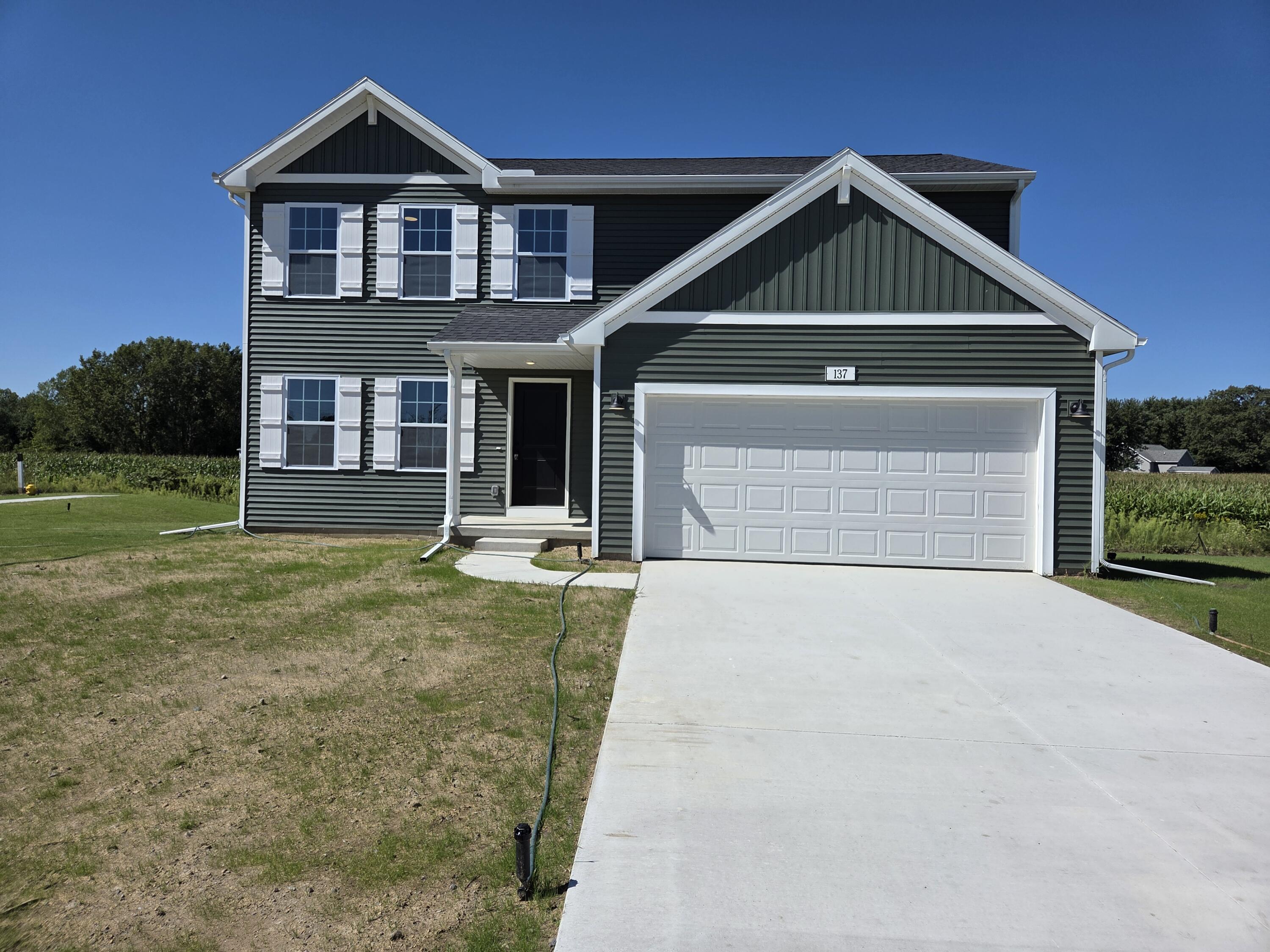 Two-story dark green house with white trim, double garage, and wide concrete driveway.