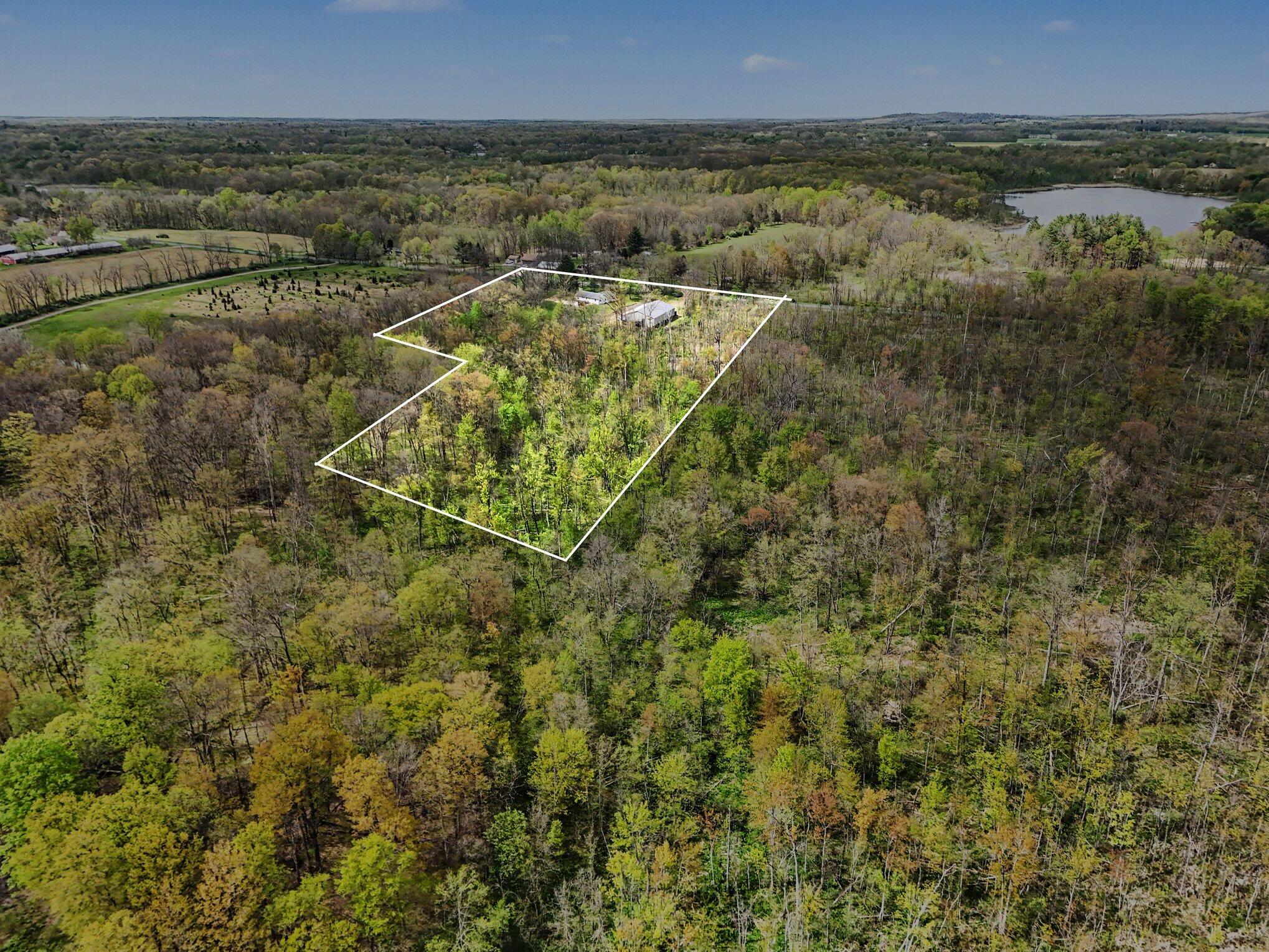 Aerial view of a wooded parcel outlined in white, with buildings and a lake beyond the trees.