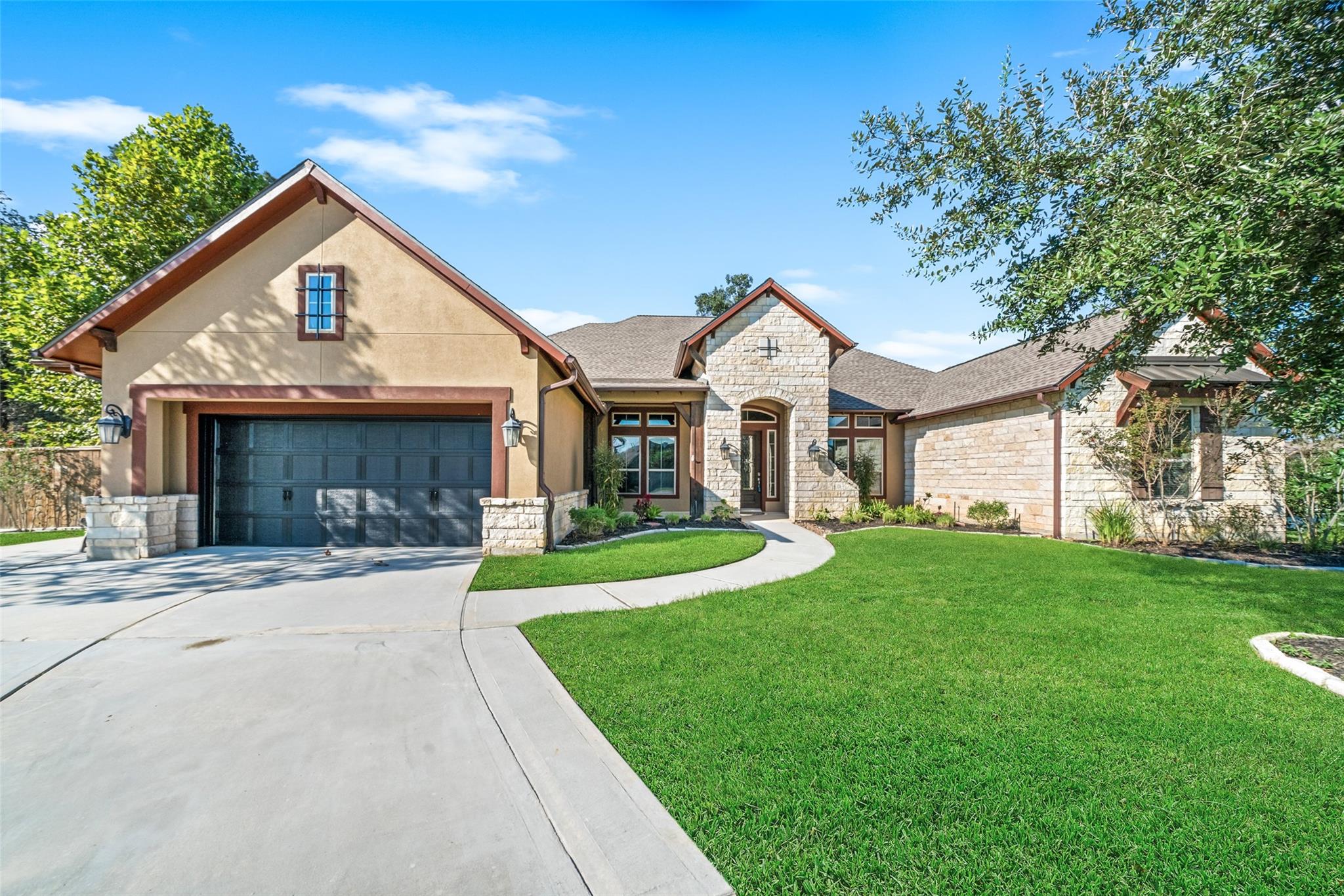 Single-story stucco and stone home with a double garage, green lawn, and curved entry walkway.