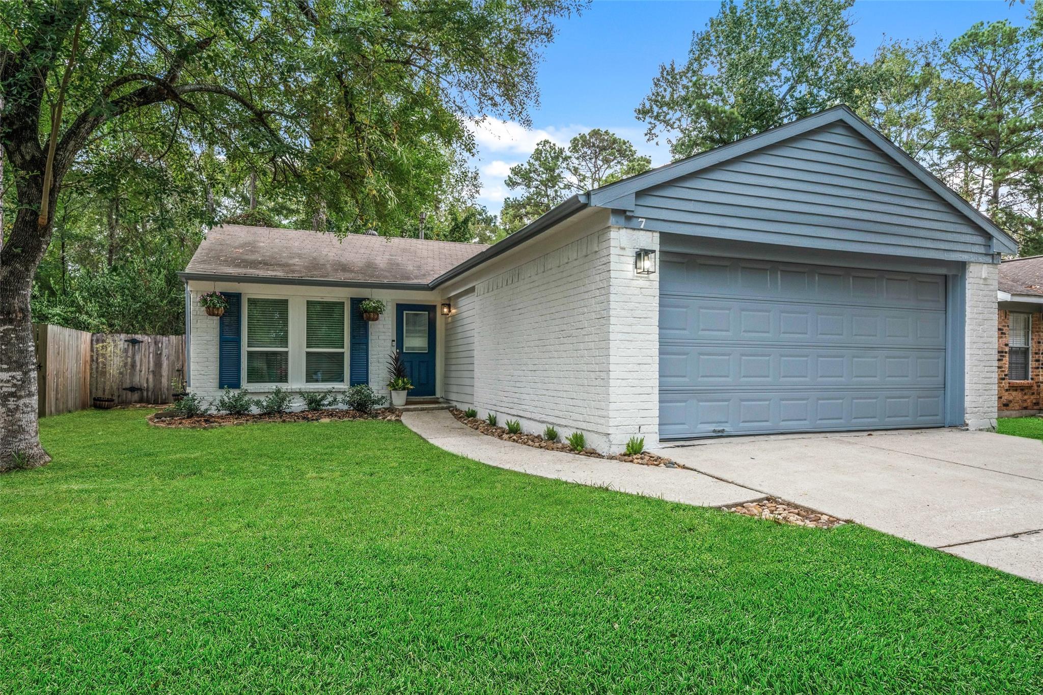 White-brick house with a blue double garage door, green lawn, and mature trees.