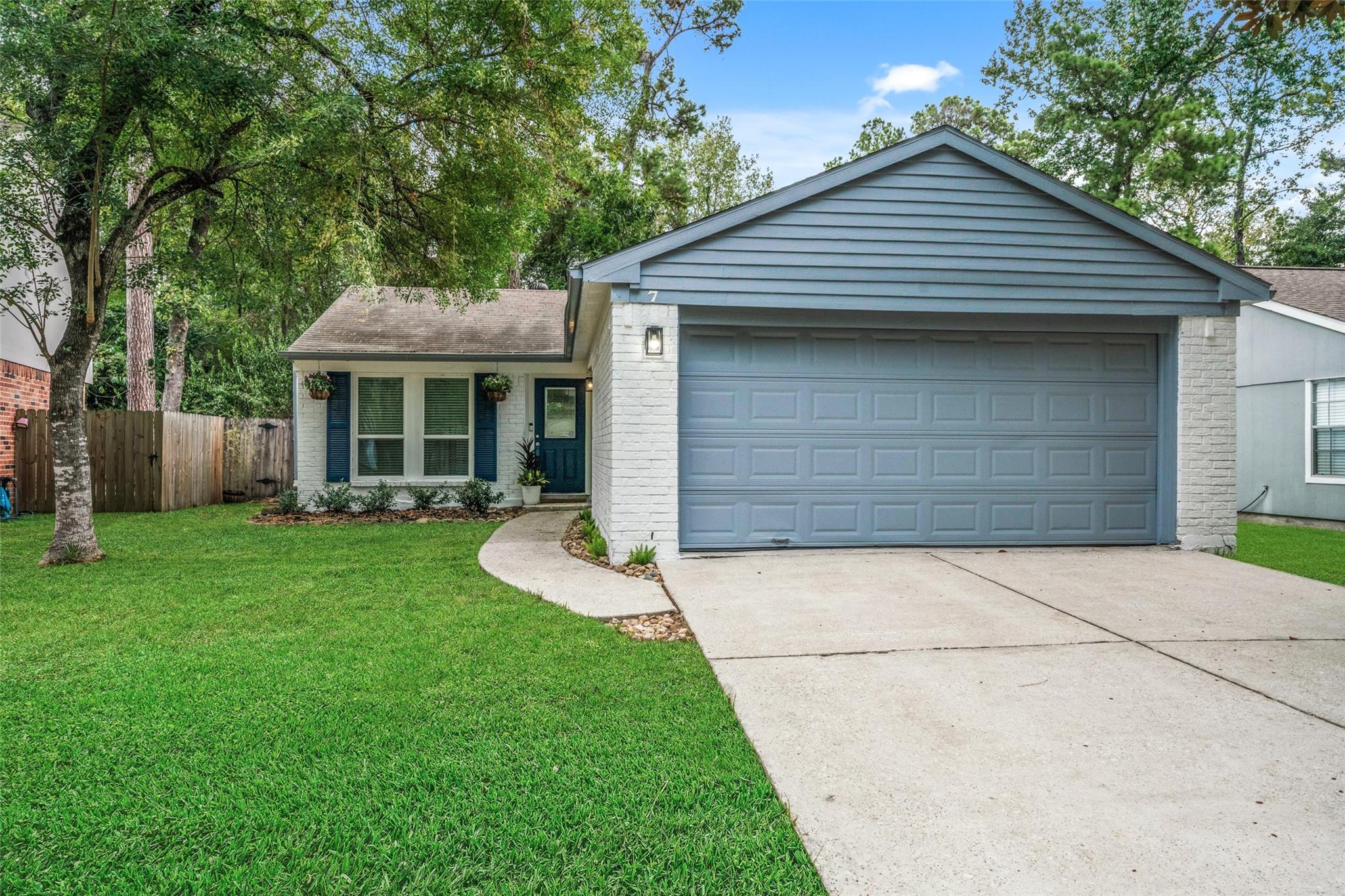 White-brick home with blue-gray double garage door, curved walkway, and tree-shaded lawn.