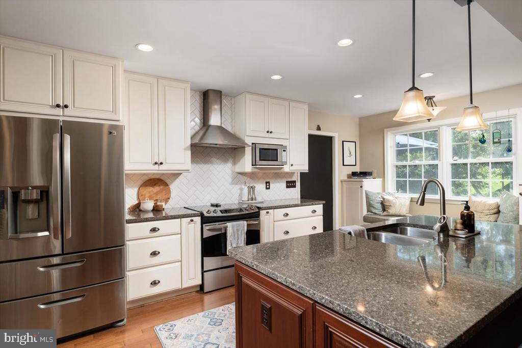 Kitchen with white cabinets, stainless steel appliances, and a large granite island beside bright windows.