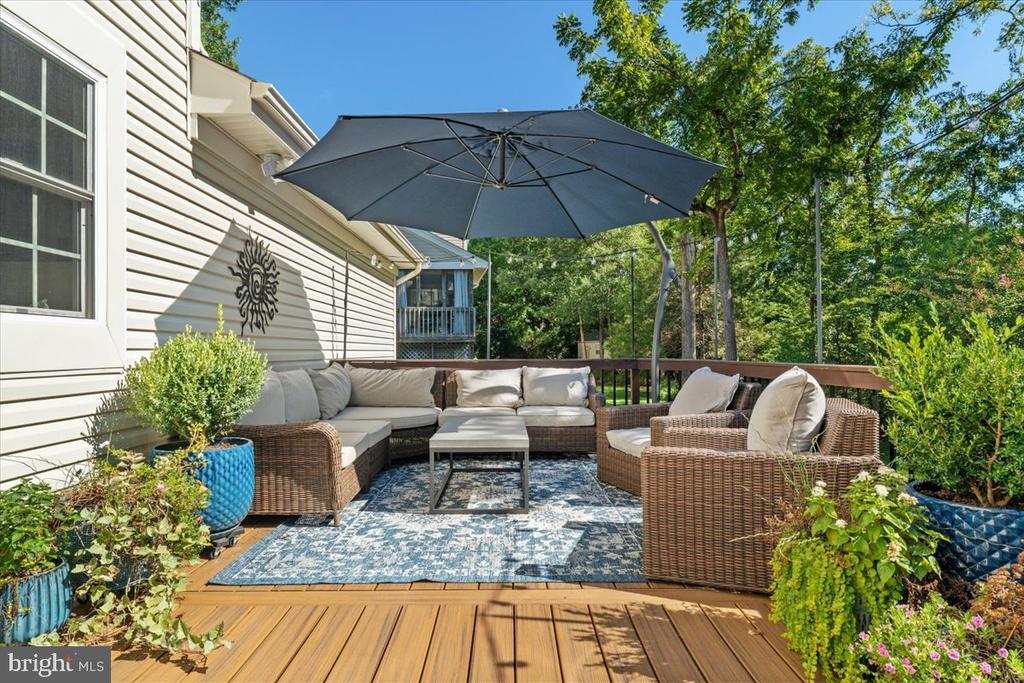 Furnished deck with wicker seating, a large umbrella, patterned rug, and potted plants.