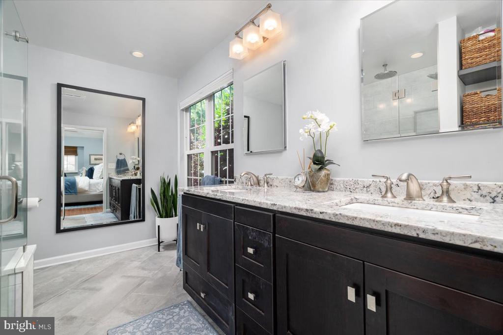 Bright bathroom with a long double-sink vanity, marble counters, and a glass-enclosed shower.