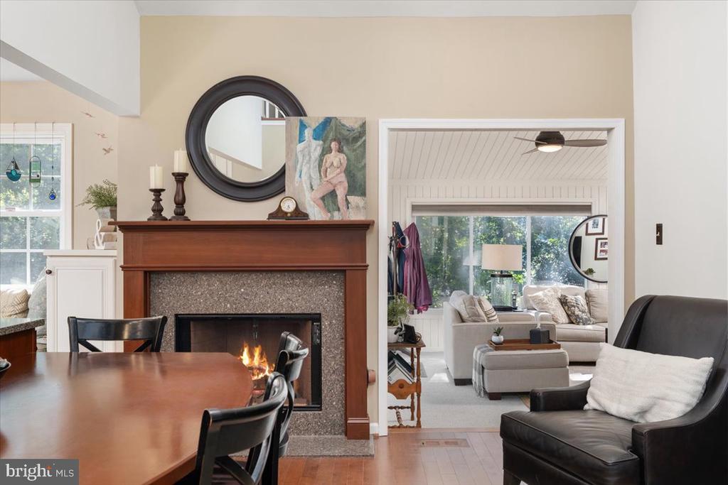 Dining and living area with a wood-mantel fireplace, dining table, and adjoining bright sitting room.