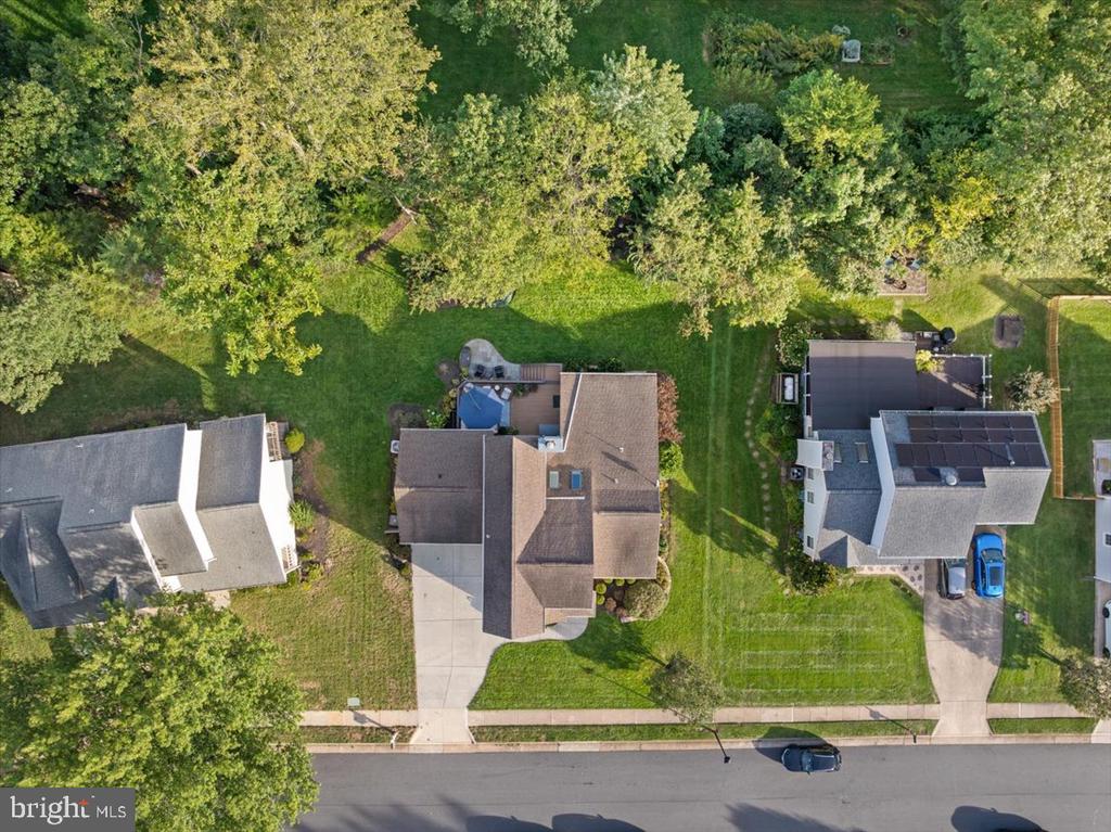 Aerial view of a house with a broad lawn, mature trees, and a patio.