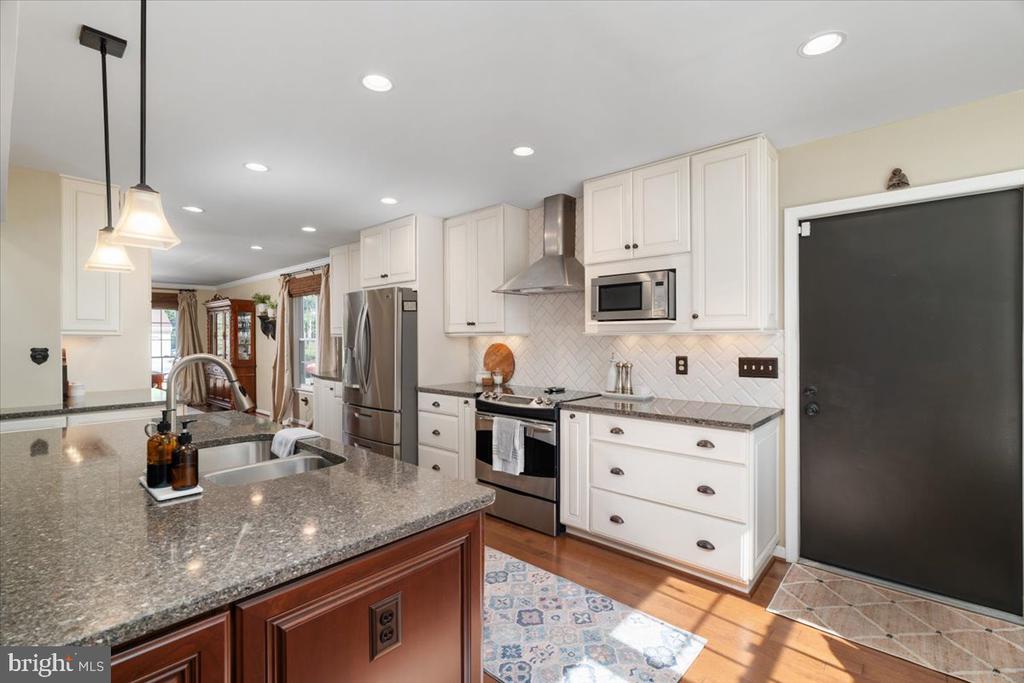 Kitchen with white cabinets, stainless steel appliances, and a granite island with a sink.