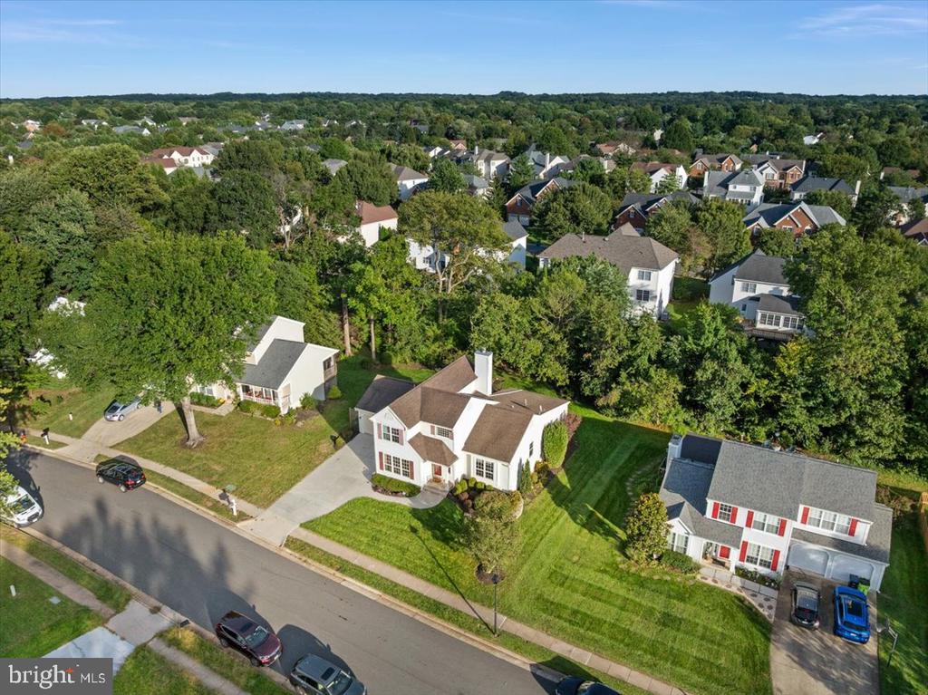 Aerial view of a white two-story home with a front lawn in a tree-lined neighborhood.