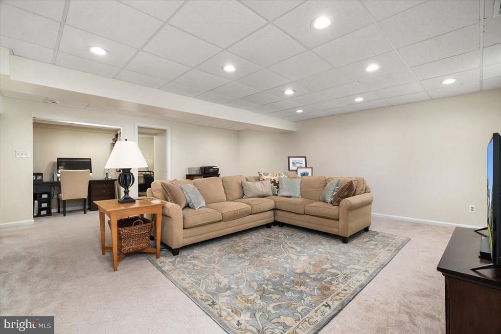 Basement family room with a beige sectional, patterned rug, and adjoining desk nook.