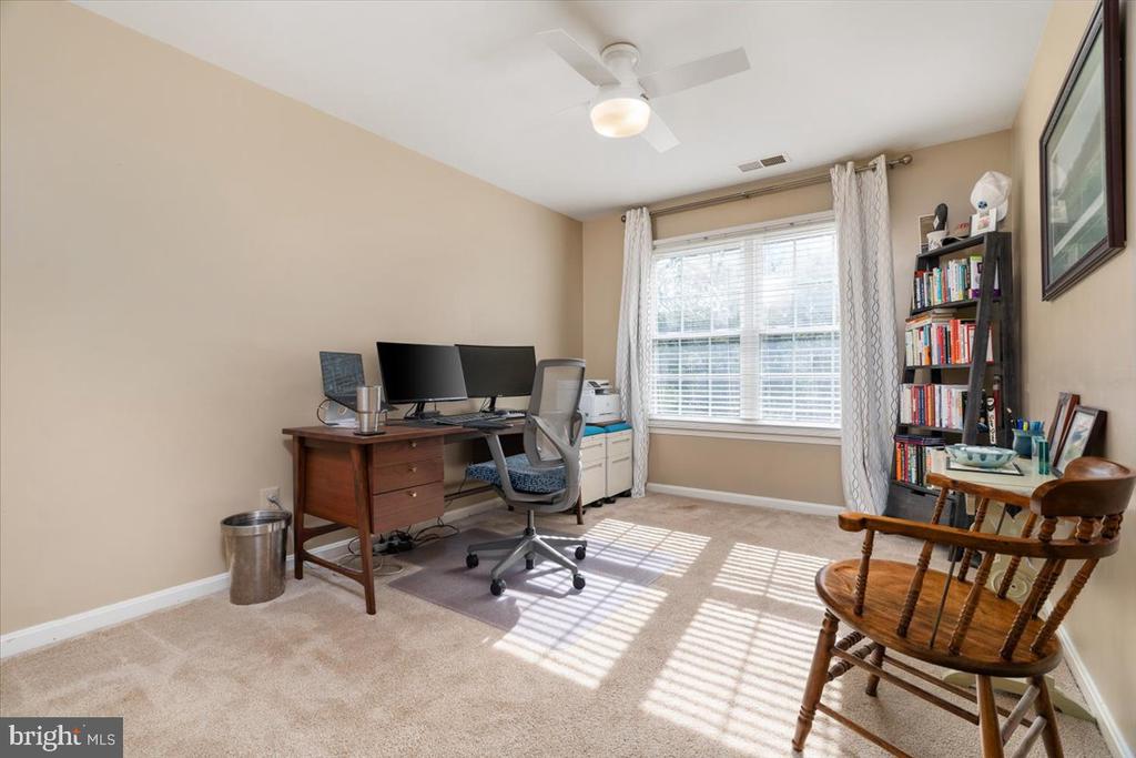 Home office with a dual-monitor desk, bookcase, and sunlight through a curtained window.