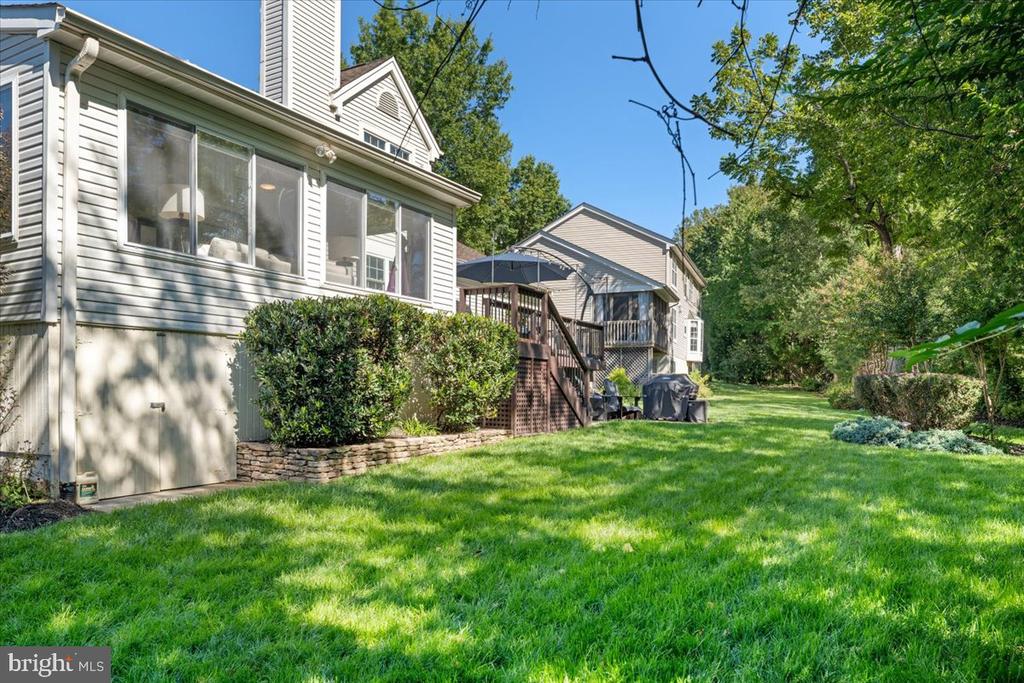 Rear of a light-sided house with a raised deck, stairs, and a spacious green lawn.
