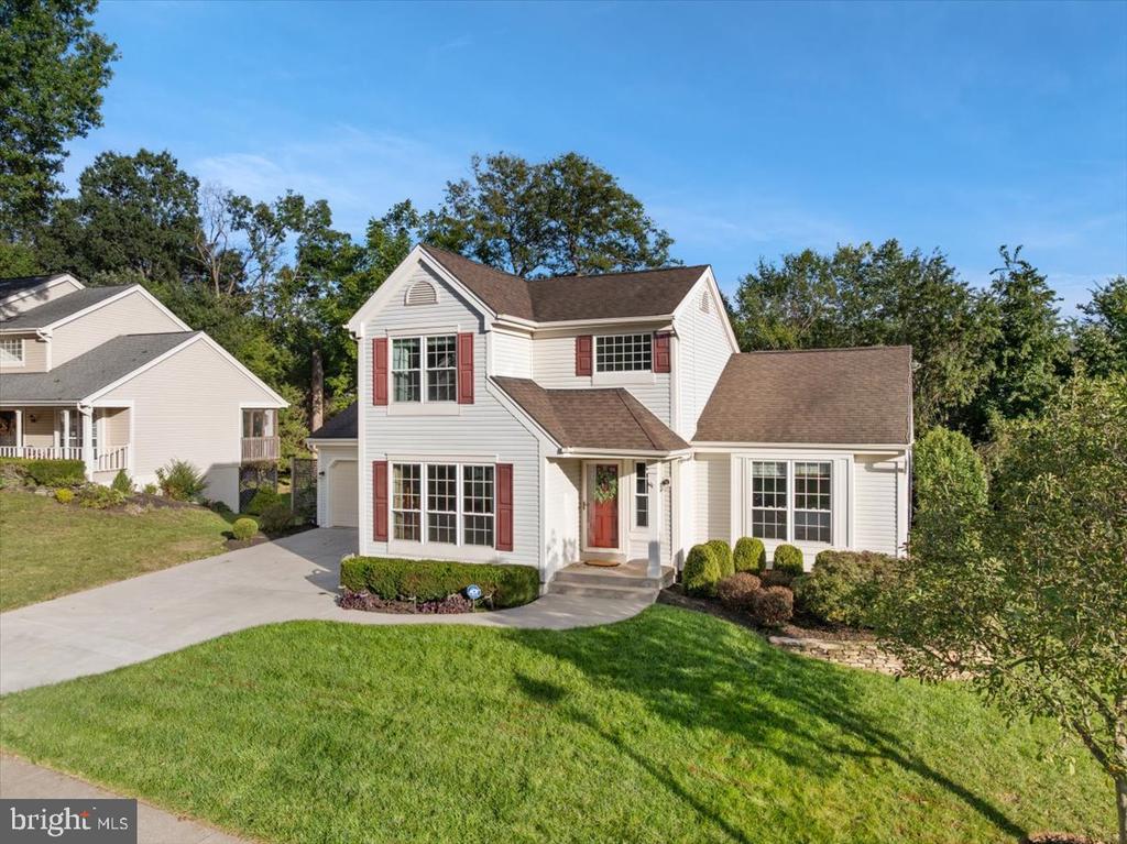 White two-story house with red shutters and front door, a broad driveway, and a manicured lawn.