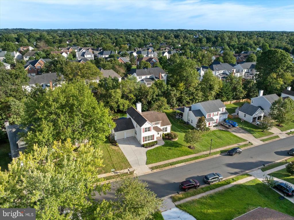 Aerial view of a two-story house with a front lawn, driveway, and tree-lined neighborhood.