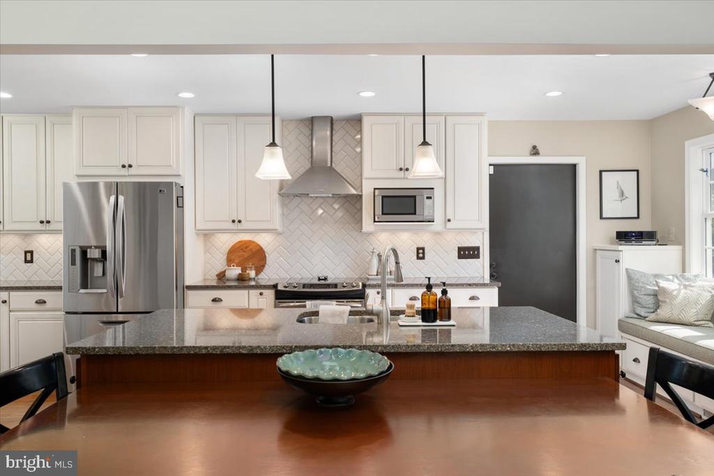 Kitchen with white cabinets, stainless steel appliances, and a gray stone island behind a dark wood table.