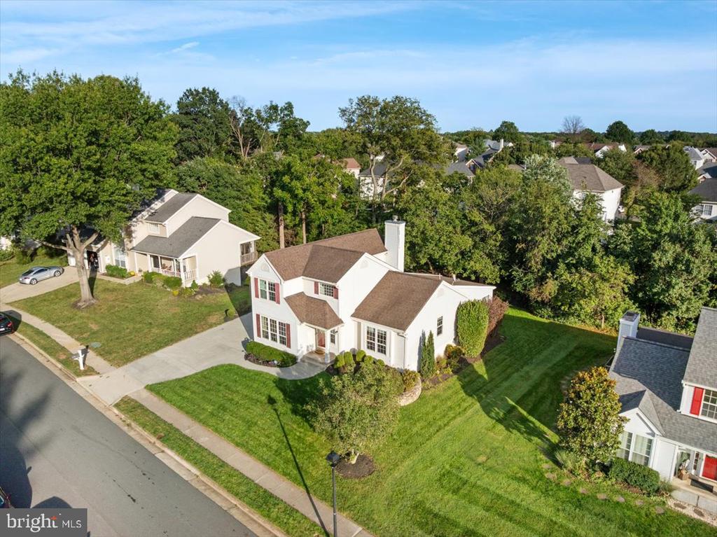 Aerial view of a white two-story house with a gray roof, broad lawn, and neighboring homes.