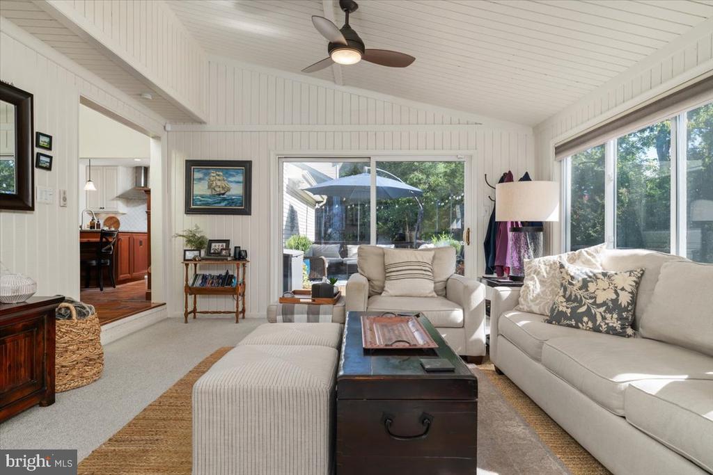 Sunroom living area with cream sofas, a trunk coffee table, and windows overlooking a patio.