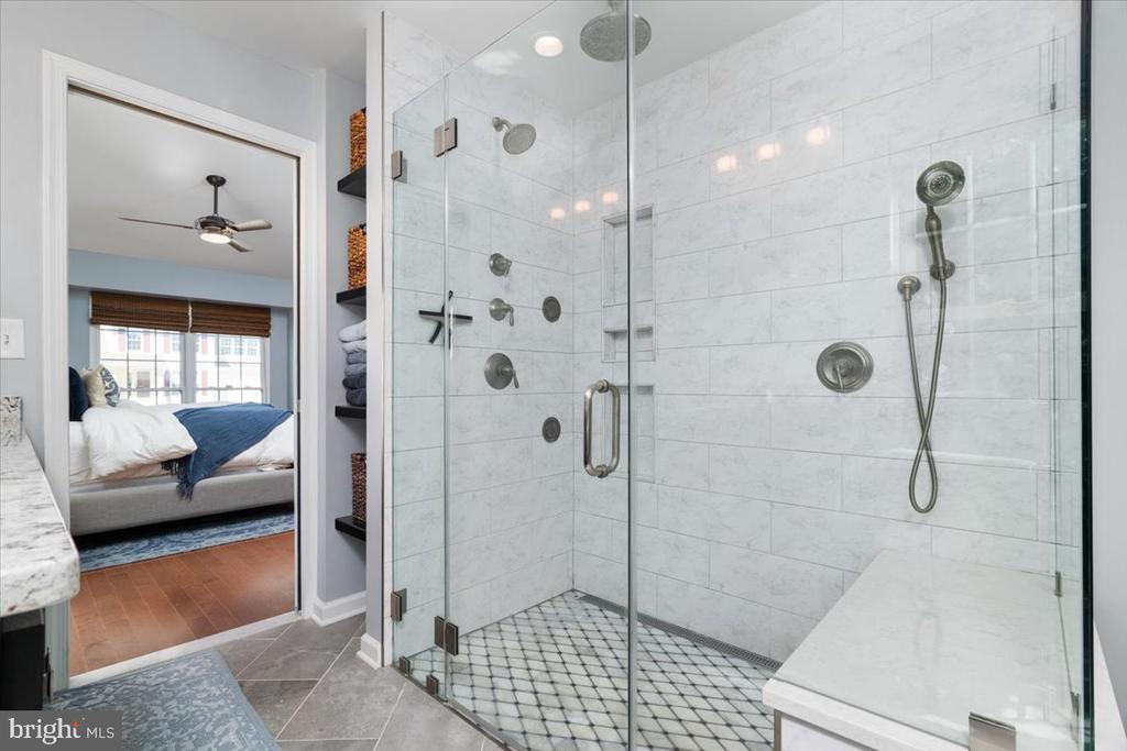 Bathroom with a glass-enclosed marble shower, multiple showerheads, and a built-in bench.