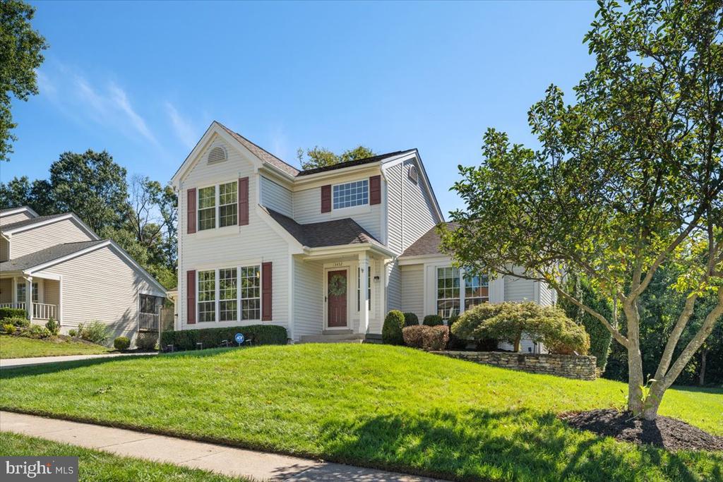 Two-story white-sided house with red shutters, a covered entry, and a sloping lawn.