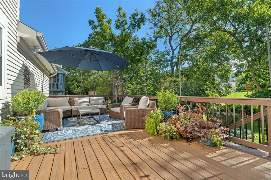 Wooden deck with wicker seating and a large umbrella overlooking leafy trees