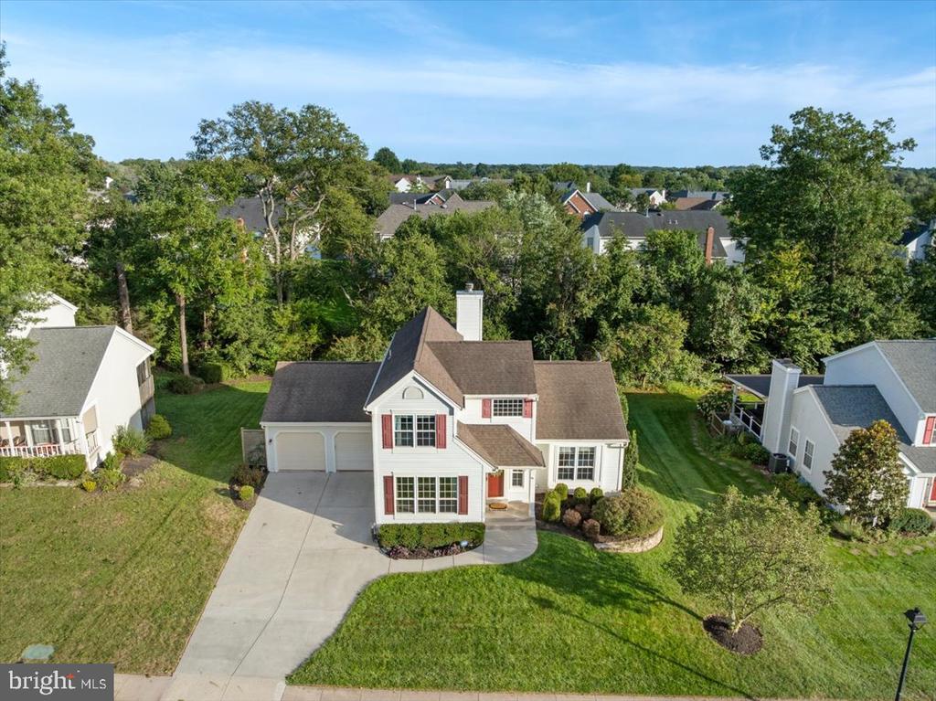Aerial view of a white two-story house with red shutters, a two-car garage, and a curved driveway.