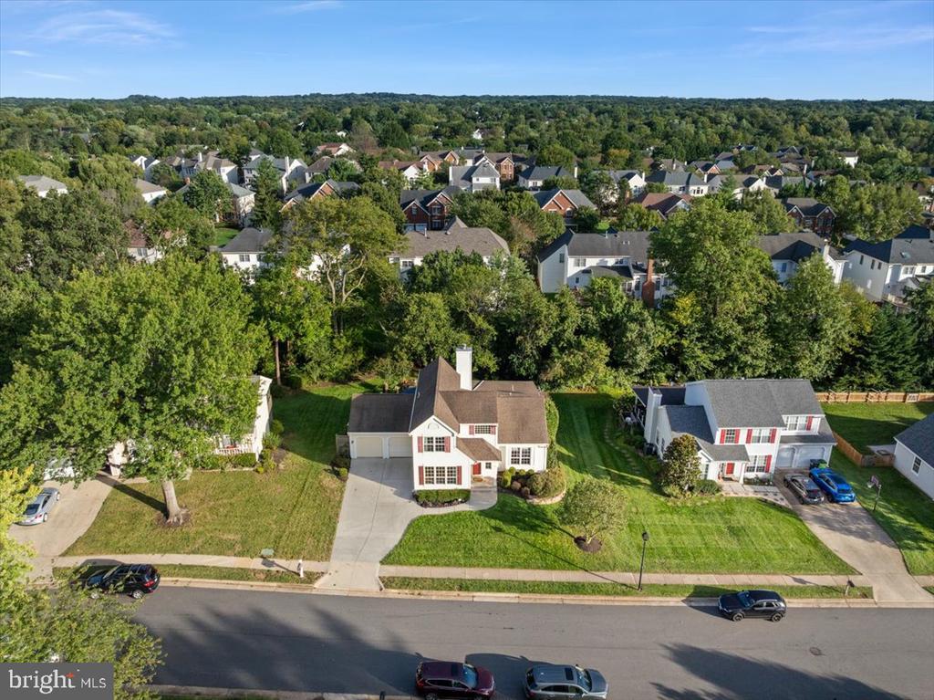 Aerial view of a two-story home with an attached garage and broad front lawn in a tree-lined neighborhood.