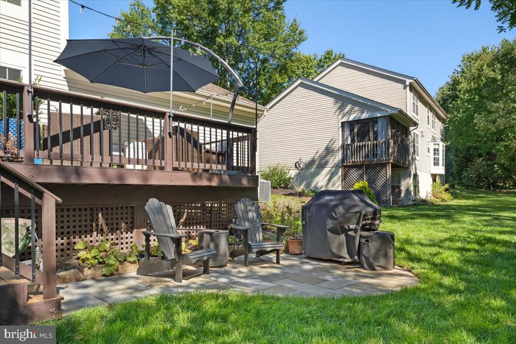 Home’s backyard with a raised deck, shaded stone patio, outdoor seating, and covered grill.