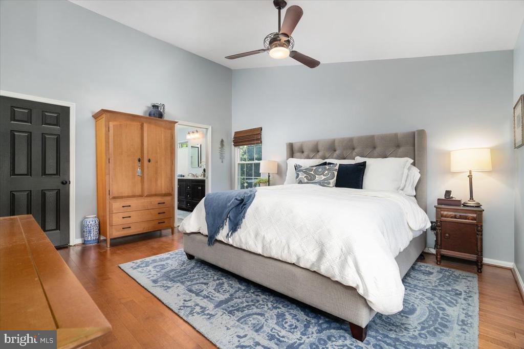 Bedroom with a large bed, tufted gray headboard, blue patterned rug, and wood wardrobe.