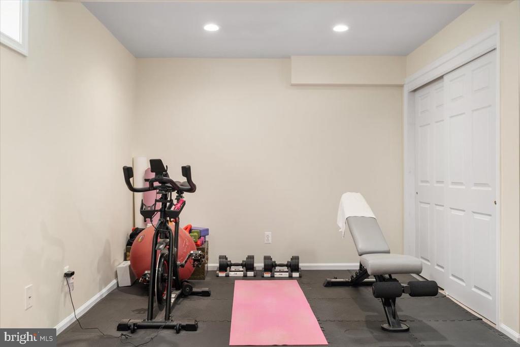 Home gym with exercise bike, weight bench, dumbbells, and a pink mat.