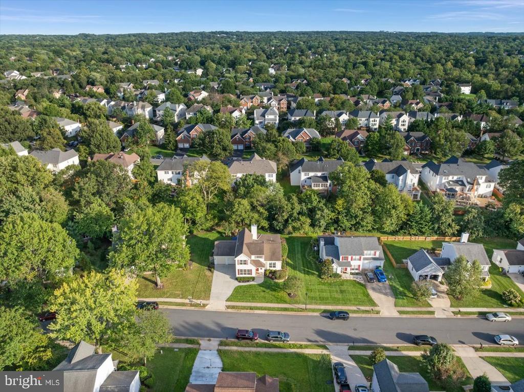 Aerial view of a detached home with a broad lawn, neighboring houses, and wooded surroundings.