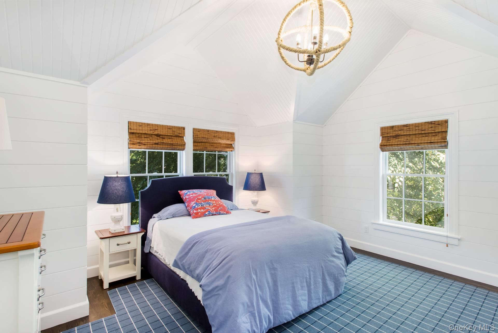 Bright bedroom with a vaulted ceiling, navy bed, blue grid rug, and woven shades.