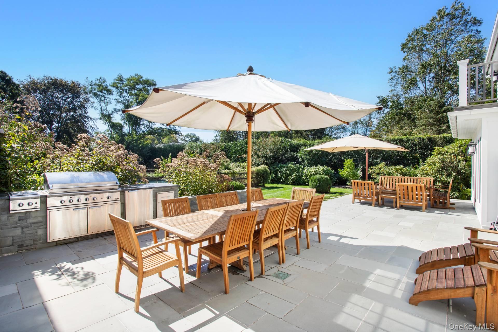Stone patio with umbrella-covered dining table, wooden seating, and built-in grill