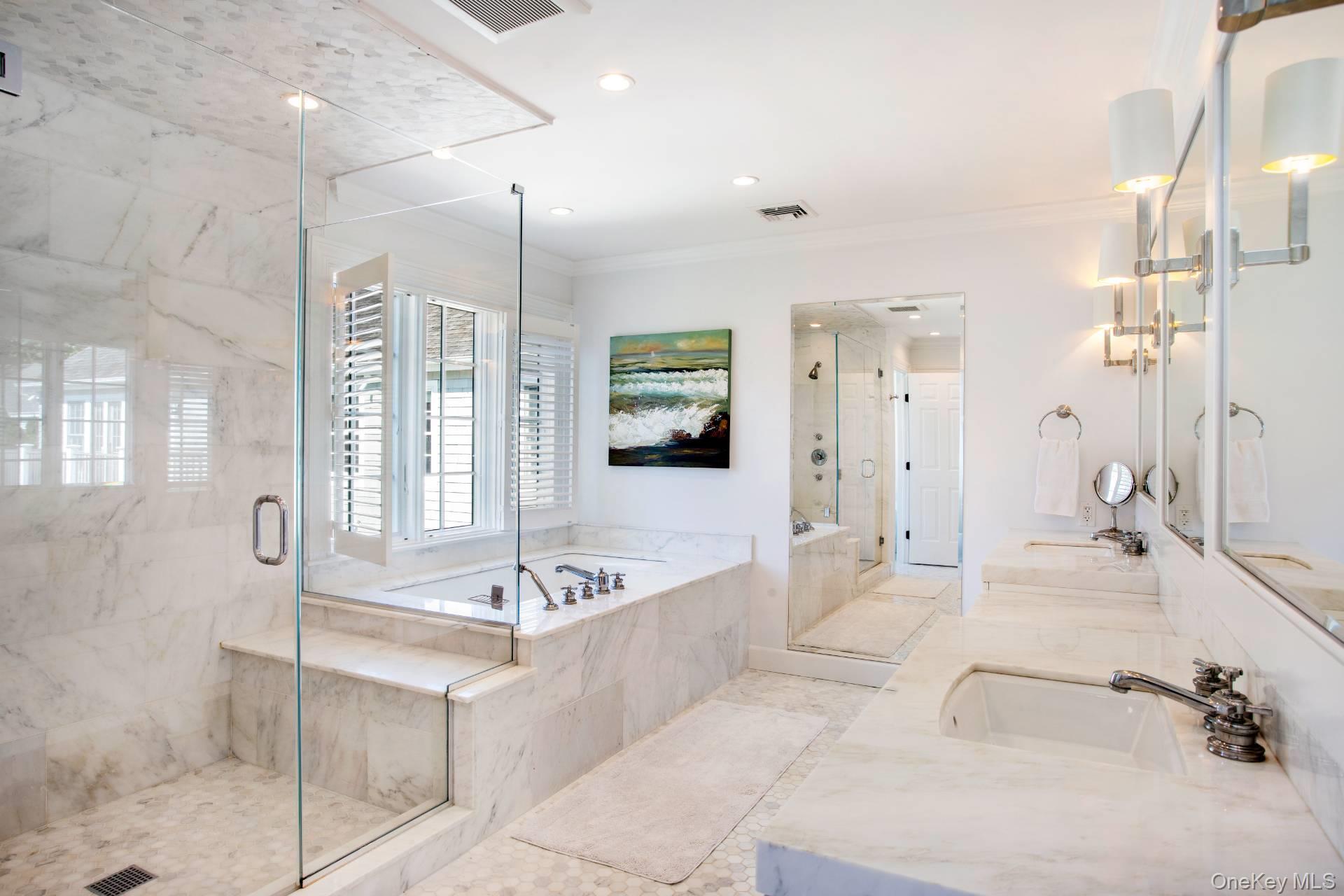 Marble bathroom with a glass-partitioned soaking tub, separate shower, and long mirrored vanity.