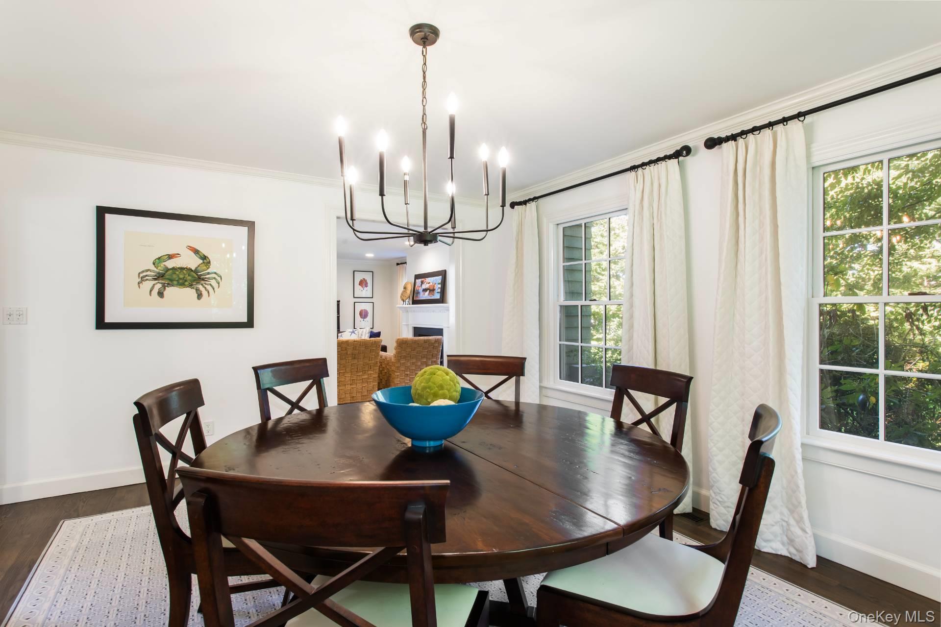 Dining room with a dark wood table, black chandelier, and windows overlooking leafy greenery.