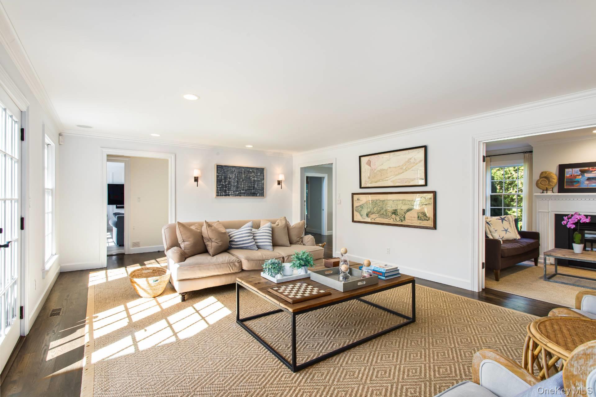 Bright living room with a beige sofa, patterned rug, and sunlight streaming through tall windows.